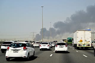 Smoke billows from an ongoing fire near Dubai International Airport as vehicles drive on a highway in Dubai on March 16, 2026